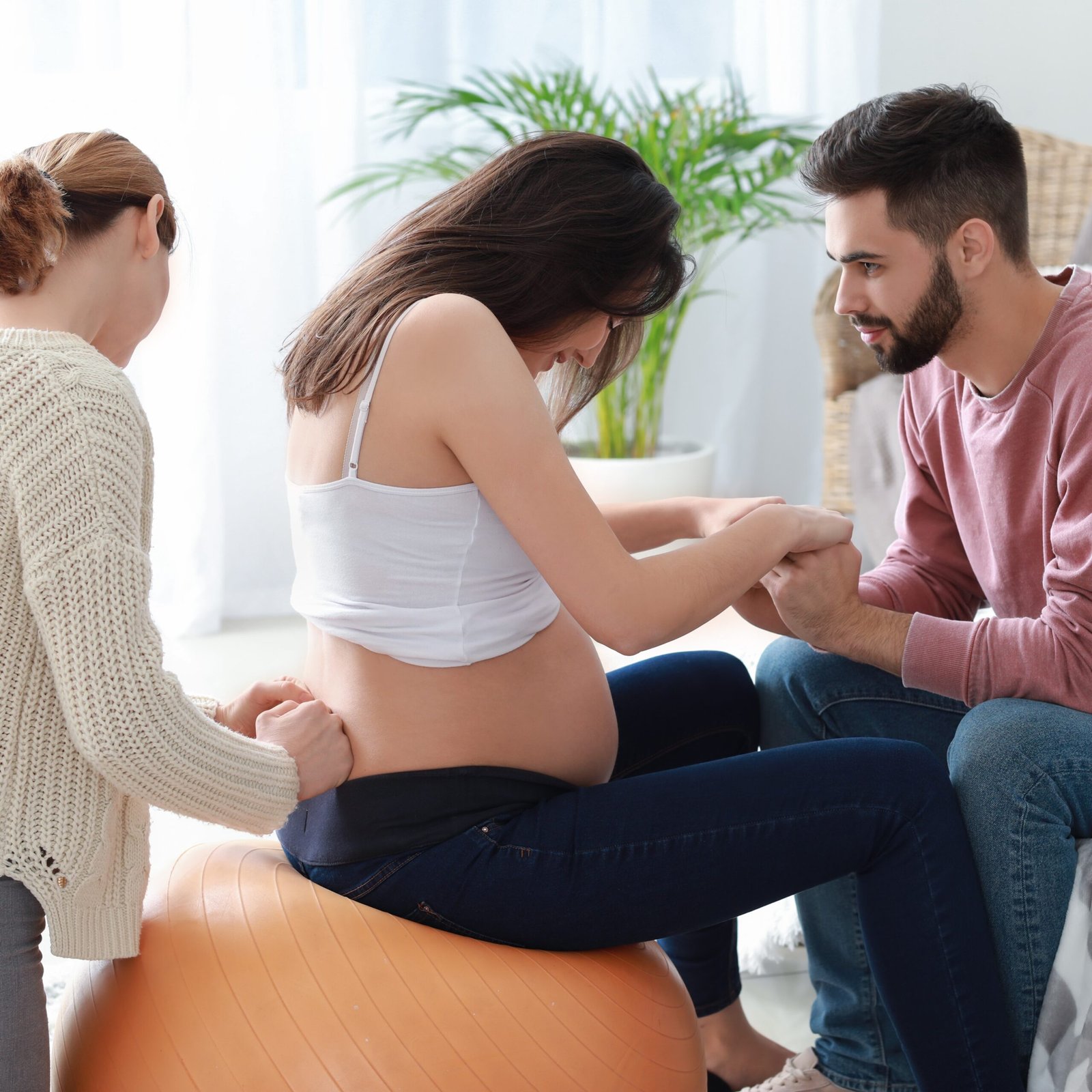 A woman in labour supported by her birth partner and a doula on a birthing ball