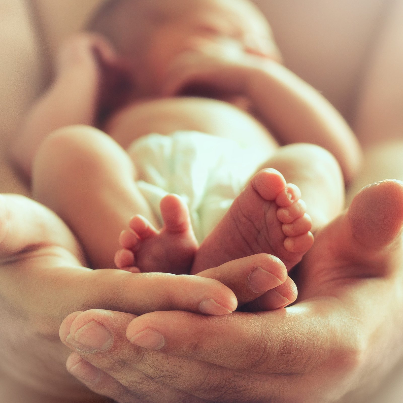 A sleeping newborn baby being held in male hands