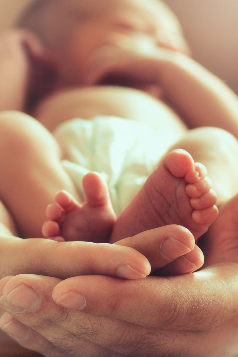 Male hands hold a newborn baby, cupping its feet